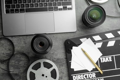 Photo of Flat lay composition with movie clapper, film reel and camera lens on grey textured table