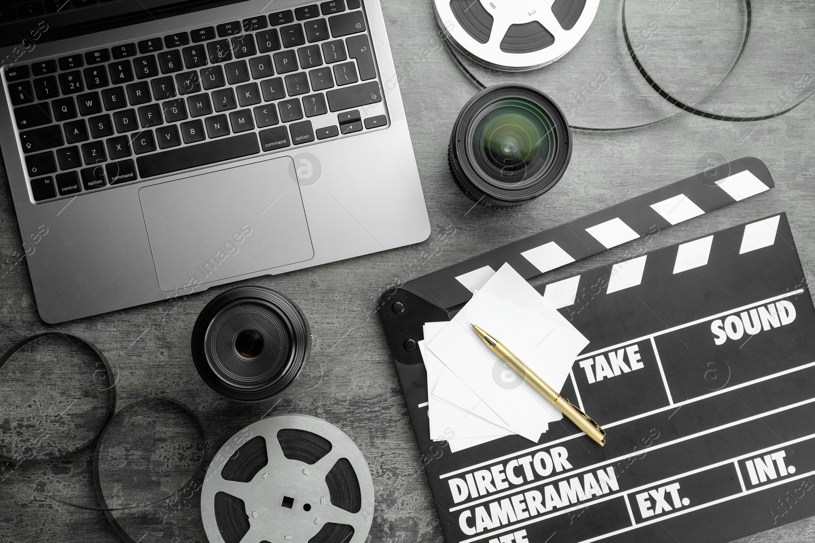 Photo of Flat lay composition with movie clapper, film reels and camera lens on grey textured table