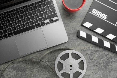 Photo of Flat lay composition with movie clapper, film reel and laptop on grey textured table