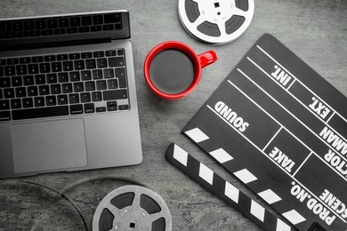 Photo of Flat lay composition with movie clapper, film reels and laptop on grey textured table