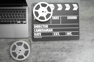 Photo of Movie clapper, film reels and laptop on grey textured table, flat lay