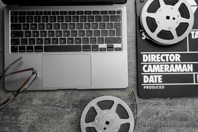 Photo of Movie clapper, film reels and laptop on grey textured table, flat lay