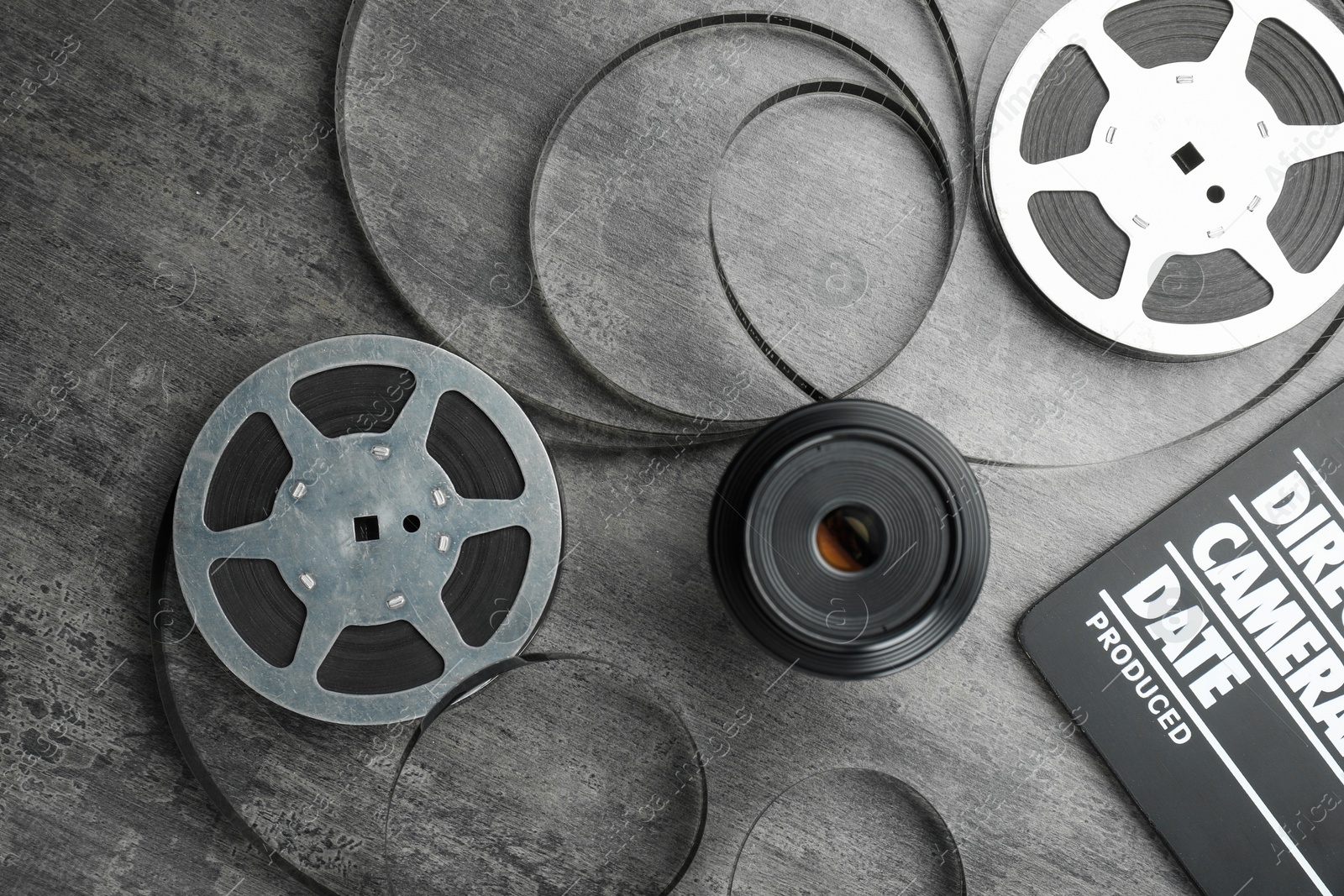 Photo of Flat lay composition with movie clapper, film reels and camera lens on grey textured table