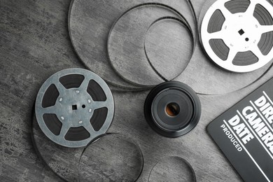 Photo of Flat lay composition with movie clapper, film reels and camera lens on grey textured table