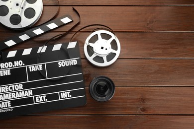 Photo of Flat lay composition with movie clapper, film reels and camera lens on wooden table. Space for text