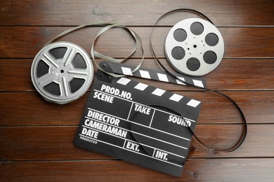 Photo of Movie clapper and film reels on wooden table, flat lay