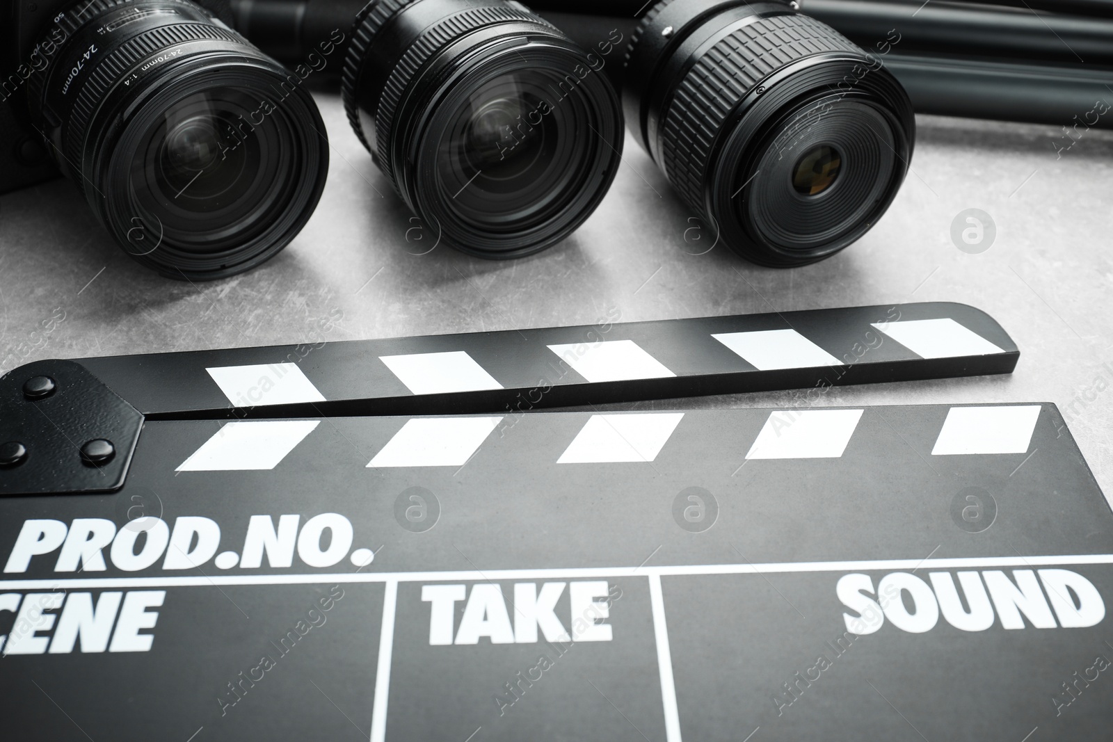 Photo of Movie clapper and camera lens on grey table, closeup