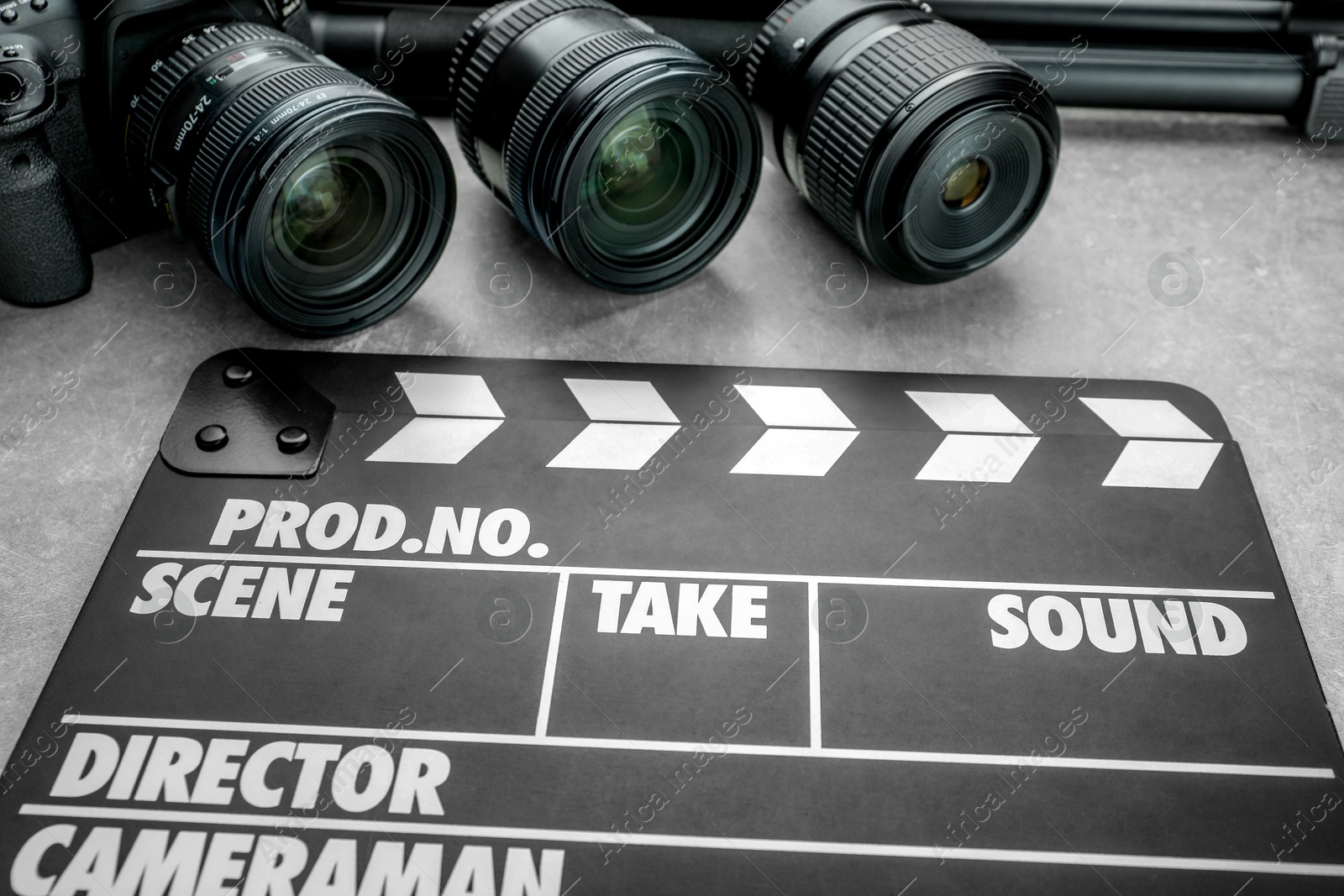 Photo of Movie clapper and camera lens on grey table, closeup