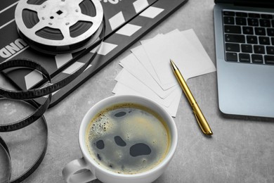 Photo of Cup of coffee, movie clapper, film reel and laptop on grey table, closeup