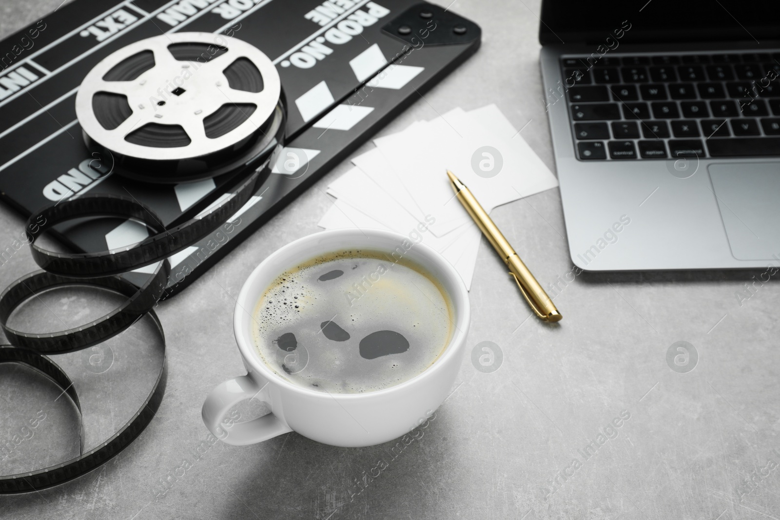 Photo of Cup of coffee, movie clapper, film reel and laptop on grey textured table