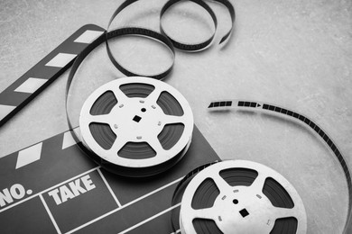 Photo of Movie clapper and film reels on grey textured table, closeup