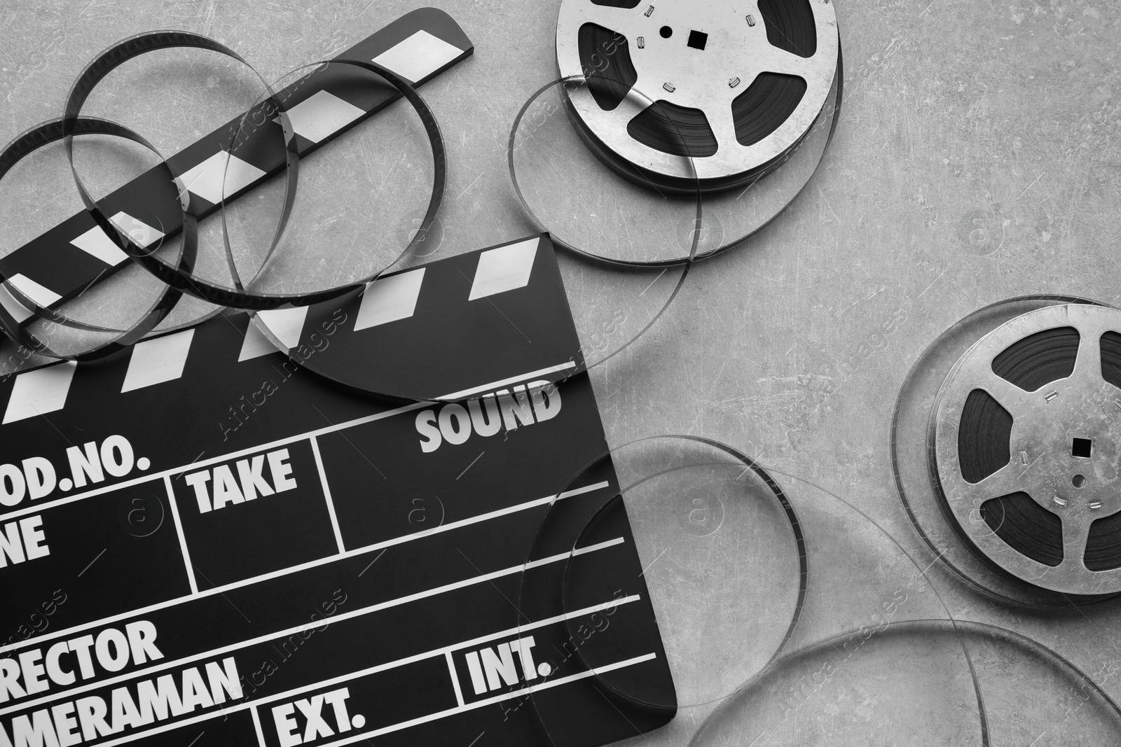 Photo of Movie clapper and film reels on grey textured table, flat lay