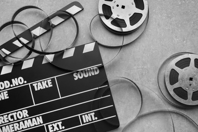 Photo of Movie clapper and film reels on grey textured table, flat lay