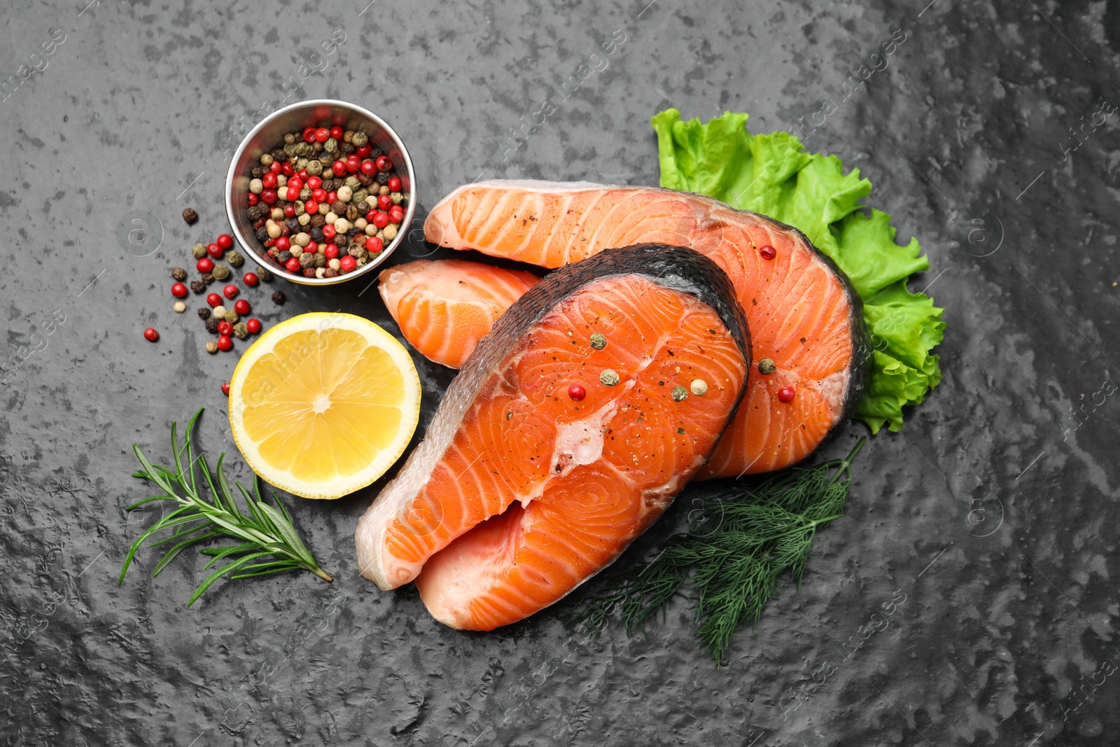 Photo of Fresh raw salmon steaks with spices and products on dark textured table, flat lay