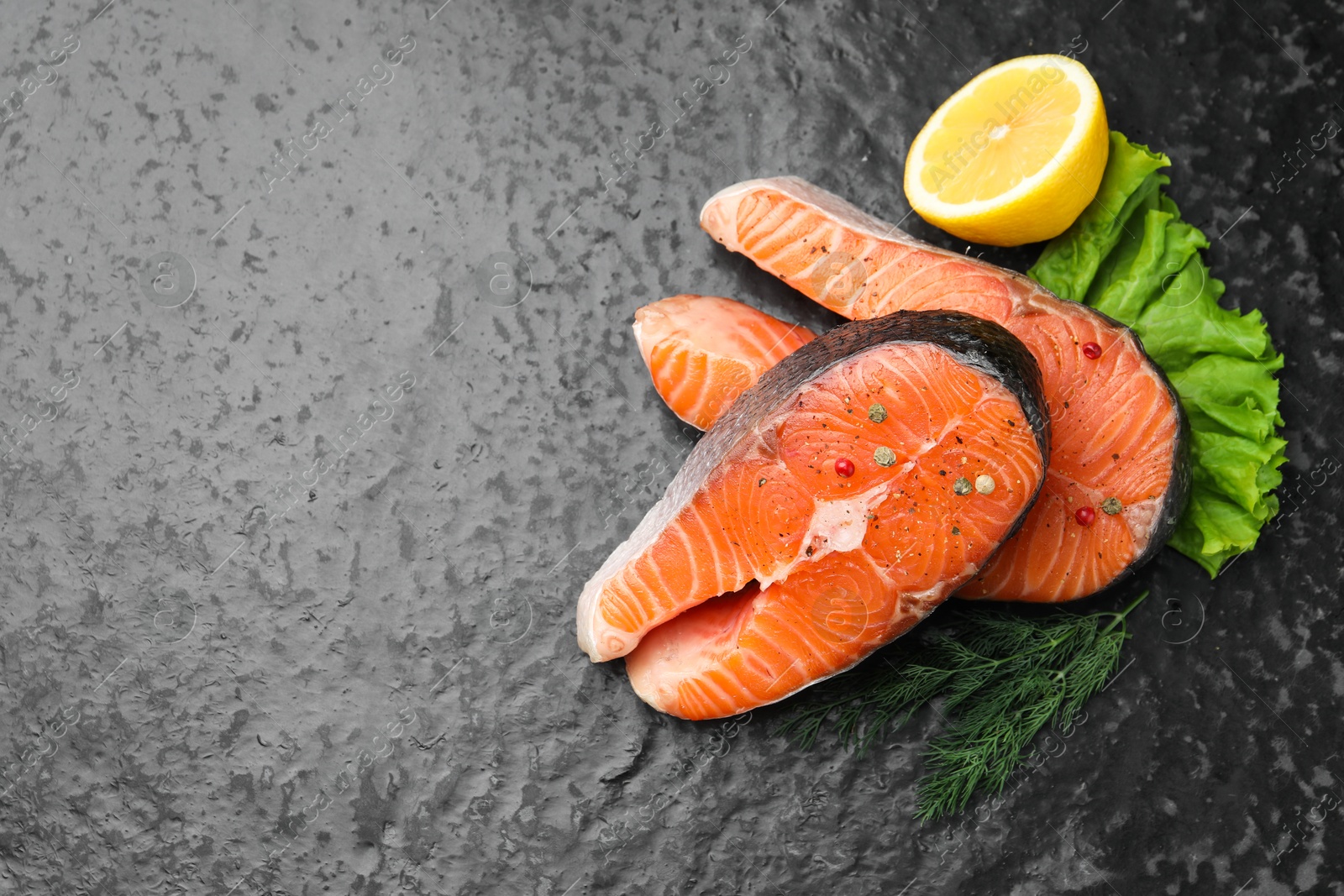 Photo of Fresh raw salmon steaks with spices, lemon, lettuce and dill on dark textured table, flat lay. Space for text