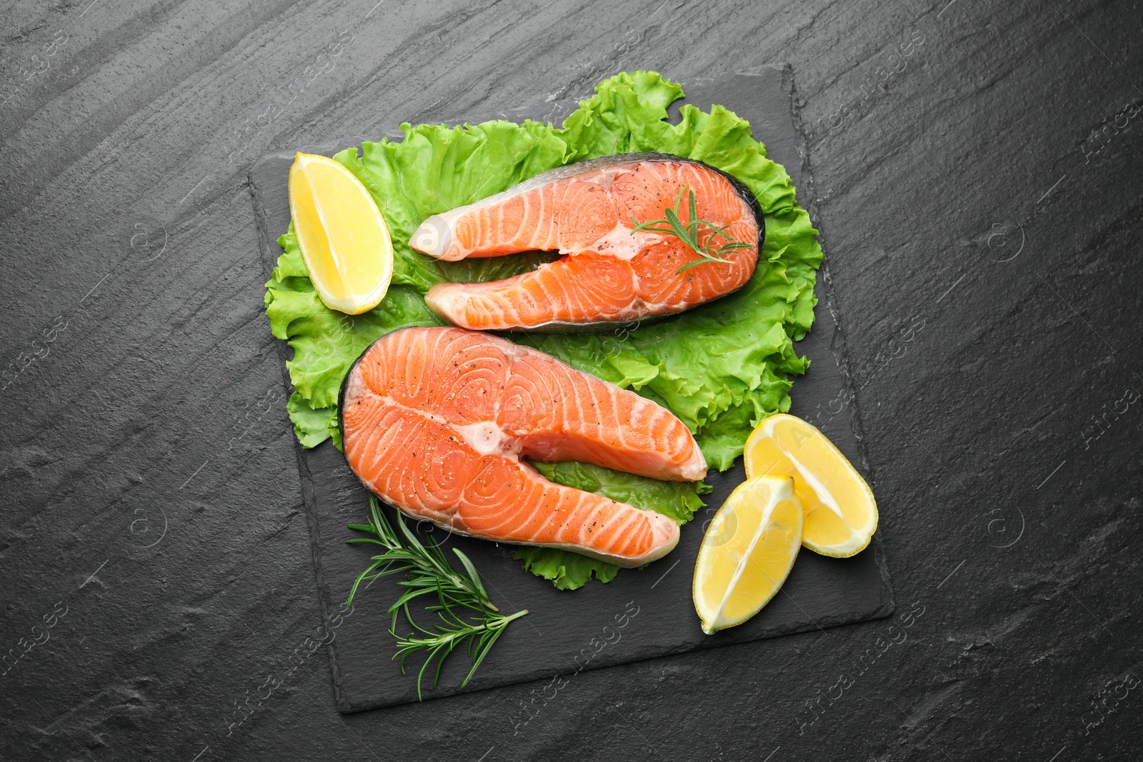 Photo of Fresh raw salmon steaks with spices, lemon, lettuce and rosemary on dark textured table, top view