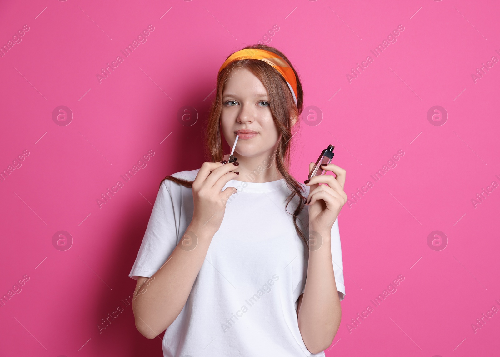 Photo of Teenage girl applying lip gloss on pink background