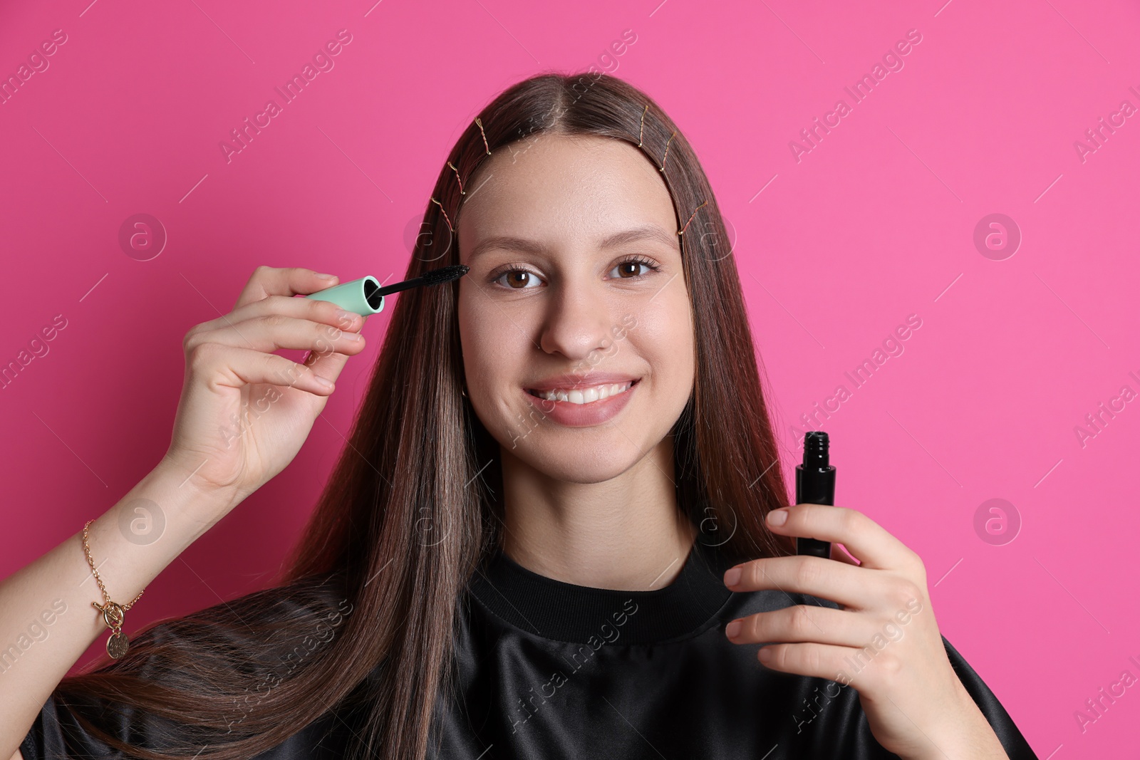 Photo of Smiling teenage girl applying mascara on pink background