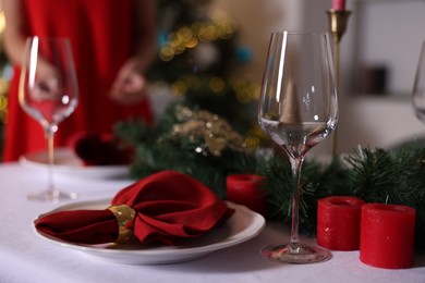 Photo of Woman setting table for Christmas dinner at home, focus on plate, glass and decor