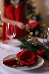 Photo of Woman setting table for Christmas dinner at home, focus on plate, napkin and decor