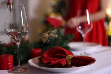 Photo of Woman setting table for Christmas dinner at home, focus on plate, glass and decor