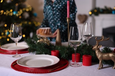 Photo of Woman setting table for Christmas dinner at home, focus on dishware, glasses and decor