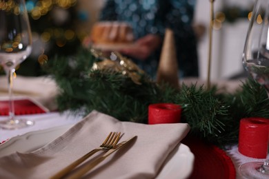 Photo of Woman setting table for Christmas dinner at home, focus on plate, cutlery and decor