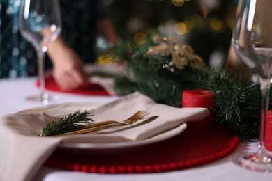 Photo of Woman setting table for Christmas dinner at home, focus on plate, cutlery and decor