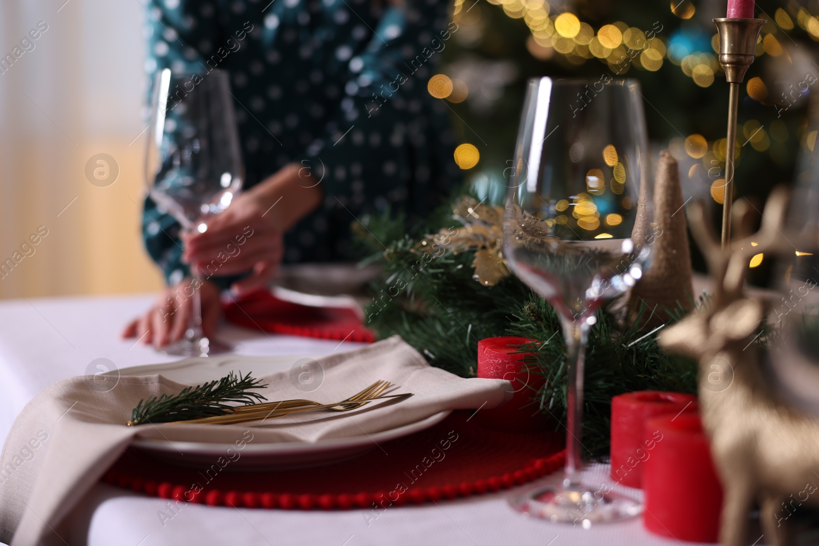 Photo of Woman setting table for Christmas dinner at home, focus on plate, cutlery and decor