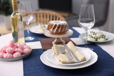 Photo of Festive table setting with dishware, desserts, wine and glasses indoors