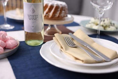 Photo of Festive table setting with dishware, cutlery, desserts and wine indoors, closeup