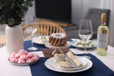 Photo of Festive table setting with dishware, desserts, wine and glasses indoors