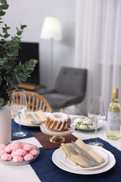 Photo of Festive table setting with dishware, desserts, wine and glasses indoors