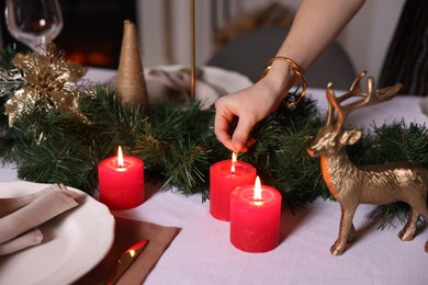 Photo of Woman lighting candle with match at table in room decorated for Christmas, closeup