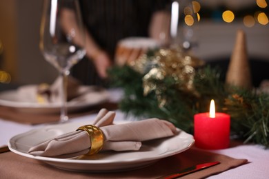 Photo of Woman setting table for Christmas dinner at home, focus on plate and decor