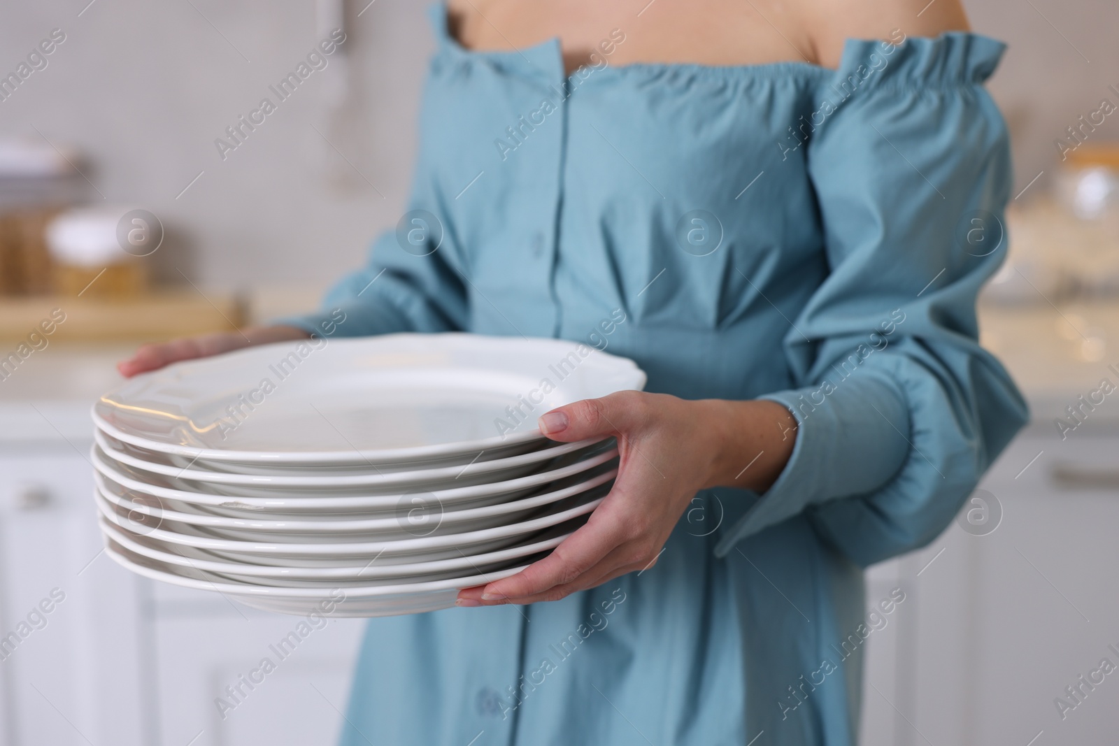 Photo of Woman with stack of plates in kitchen, closeup