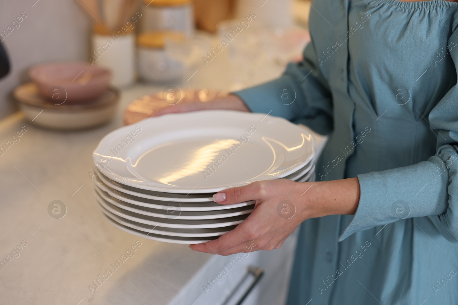 Photo of Woman with plates near countertop in kitchen, closeup