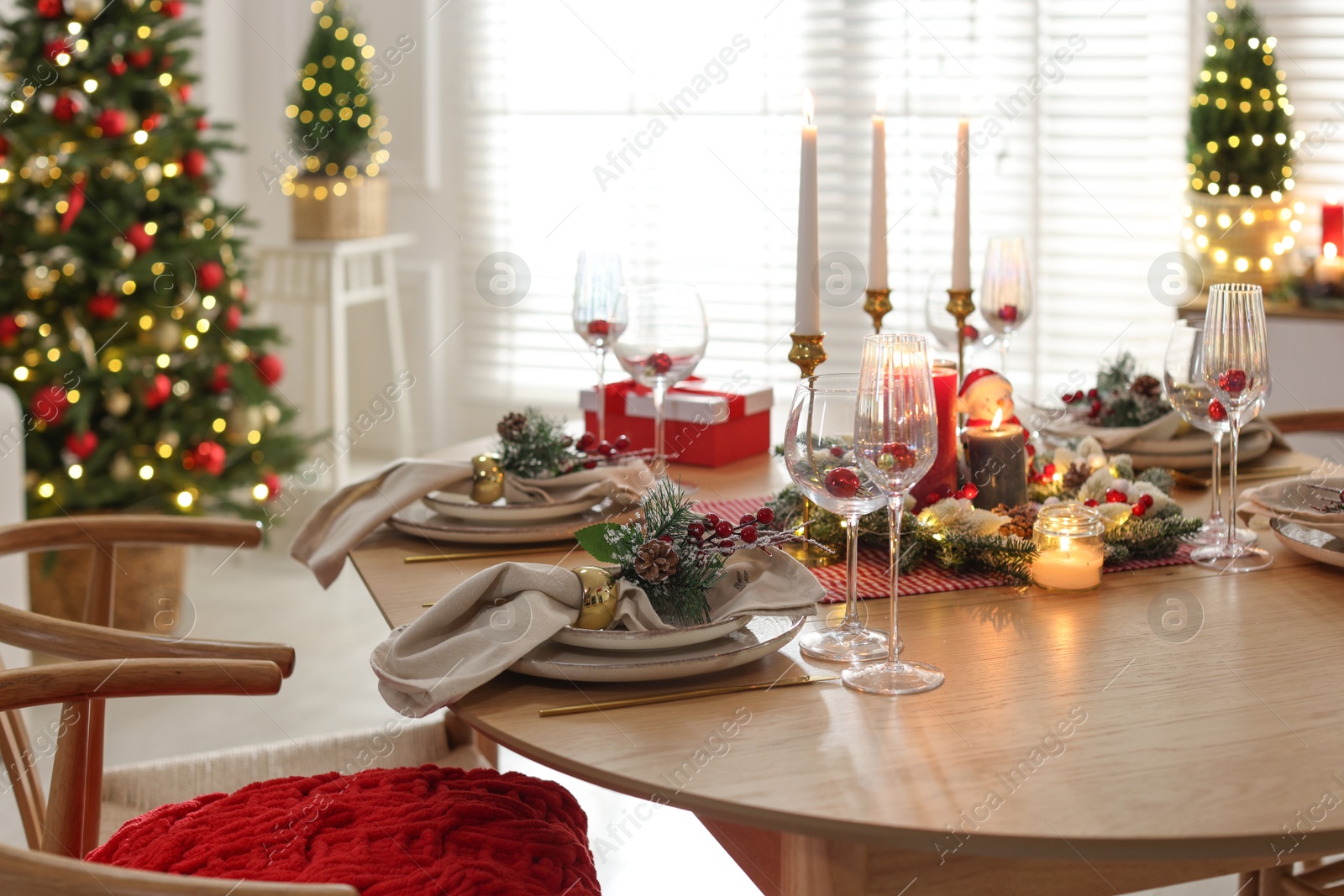 Photo of Christmas table setting with stylish dishware, glasses and burning candles in festive decorated room