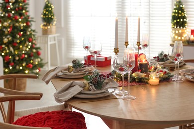 Photo of Christmas table setting with stylish dishware, glasses and burning candles in festive decorated room