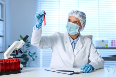 Photo of Laboratory testing. Doctor holding test tube with blood sample at table indoors