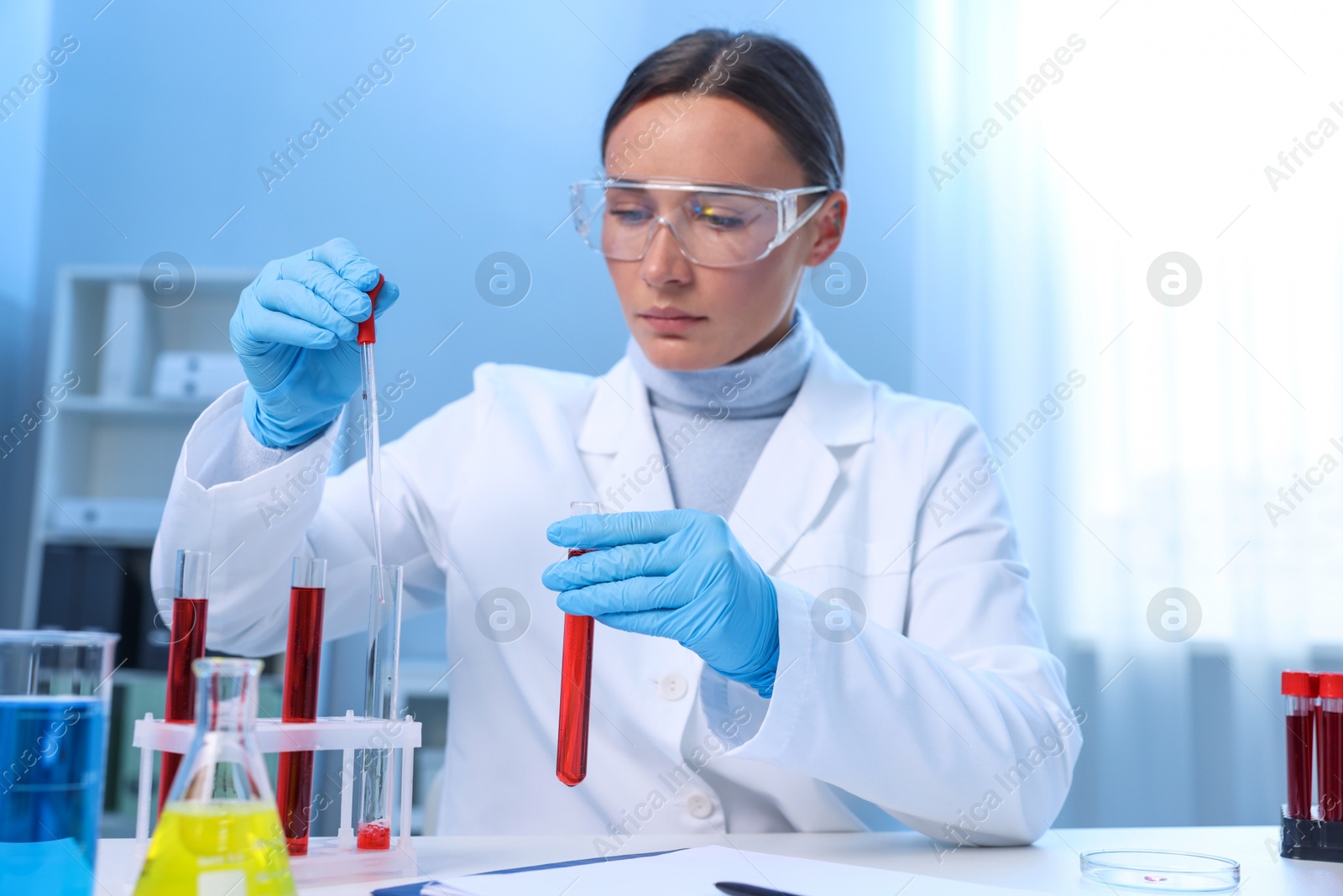 Photo of Laboratory testing. Doctor dripping blood sample into test tube at table indoors