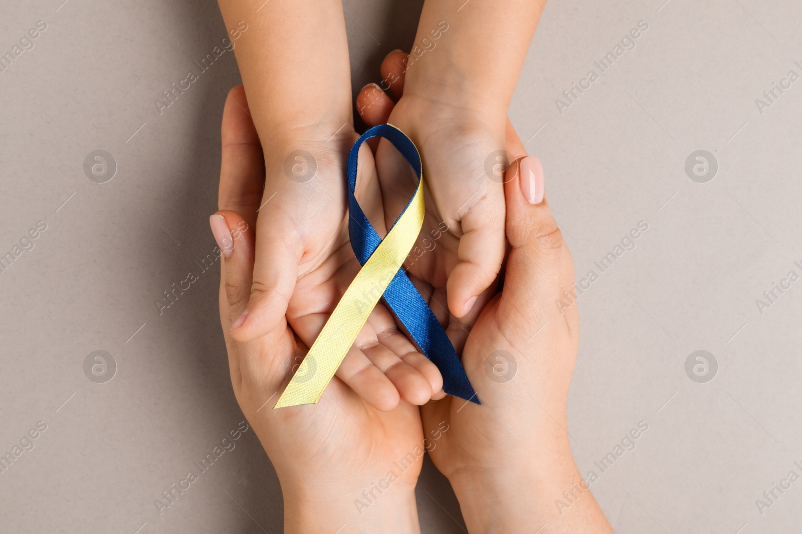 Photo of Woman with child holding yellow and blue ribbon on dark beige background, top view. Down syndrome awareness