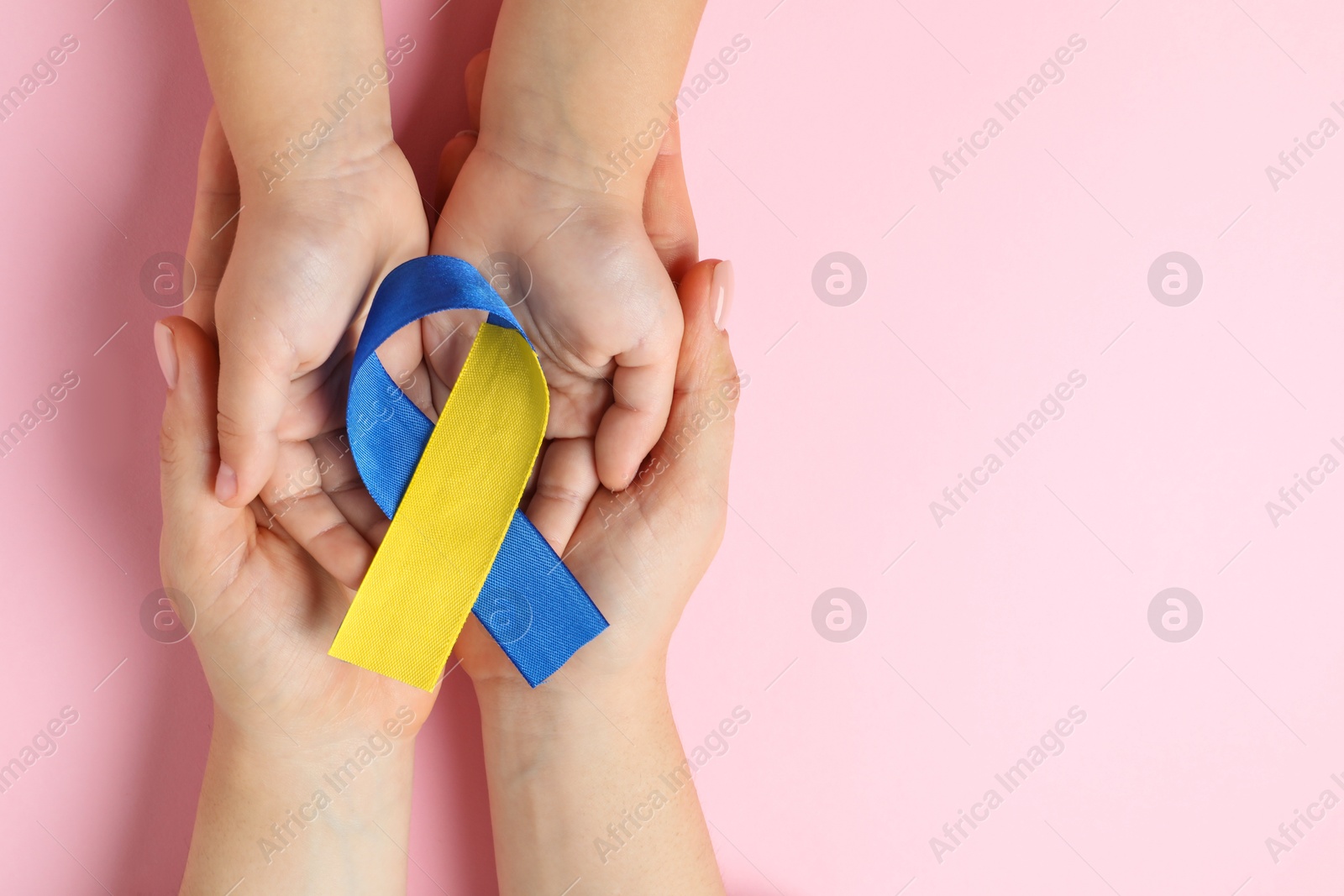 Photo of Woman with child holding yellow and blue ribbon on pink background, top view. Down syndrome awareness