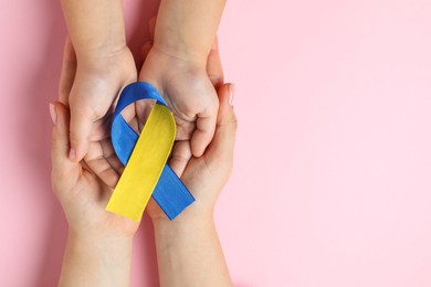 Photo of Woman with child holding yellow and blue ribbon on pink background, top view. Down syndrome awareness