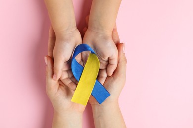 Photo of Woman with child holding yellow and blue ribbon on pink background, top view. Down syndrome awareness