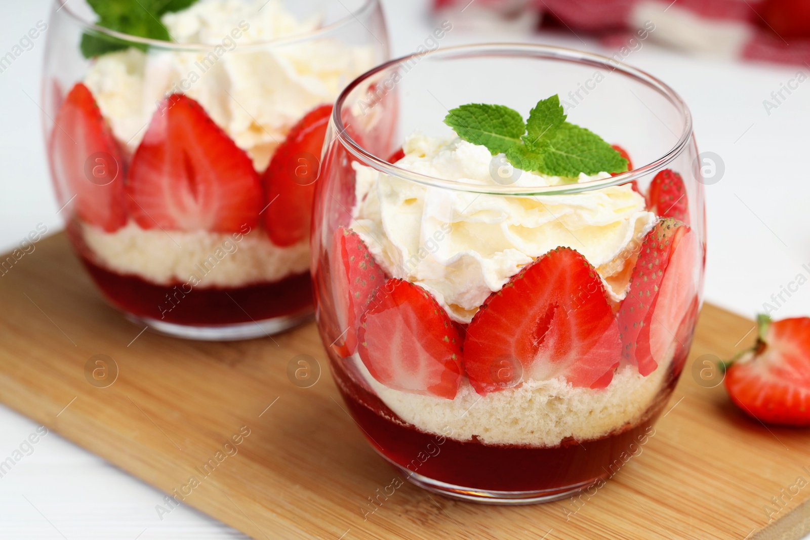 Photo of Tasty trifle dessert. Sponge cake, strawberries, jam and whipped cream in glasses on table, closeup