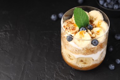 Photo of Tasty trifle dessert. Sponge cake, blueberries, banana and whipped cream in glass on black table, closeup. Space for text