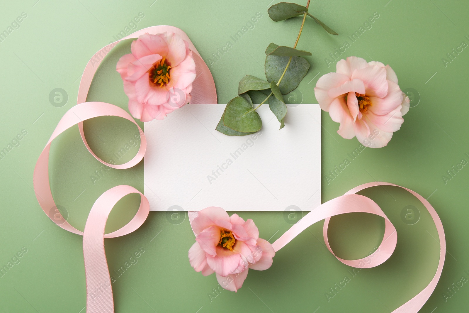 Photo of Blank card, ribbon, eustoma flowers and eucalyptus branch on green background, flat lay