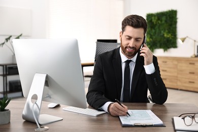 Man talking on smartphone while working at table in office