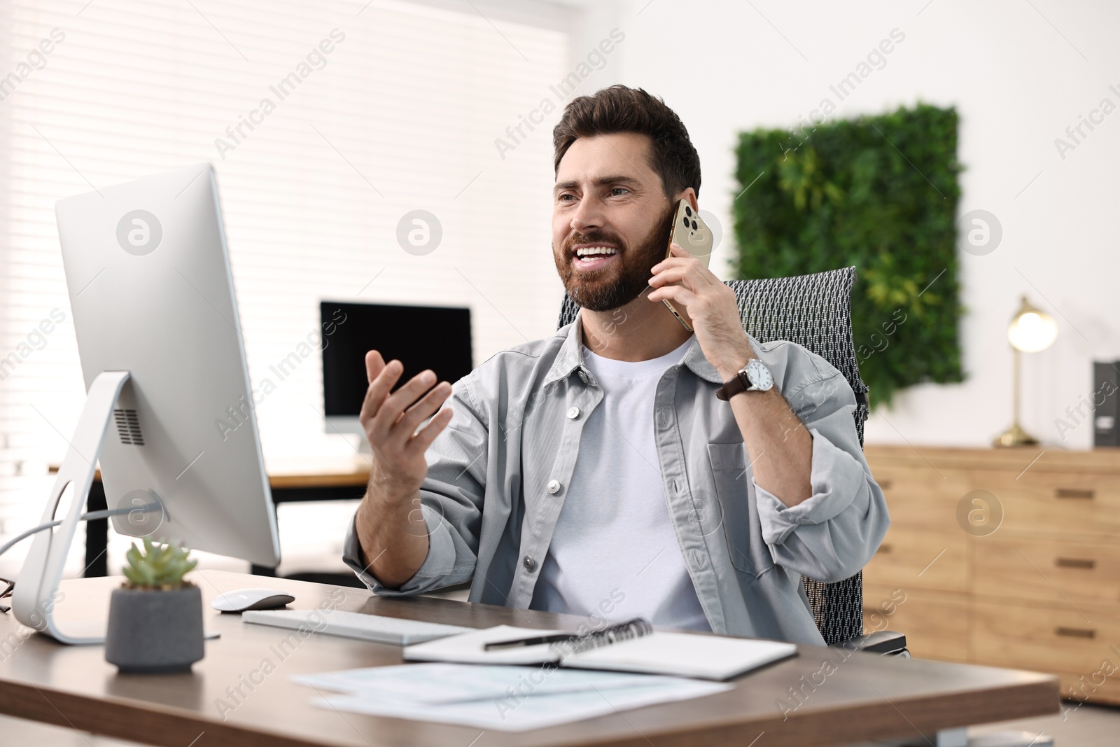 Photo of Man talking on smartphone while working at table in office